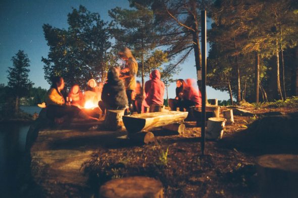 Folk som hygger seg foran bålet på kvelden